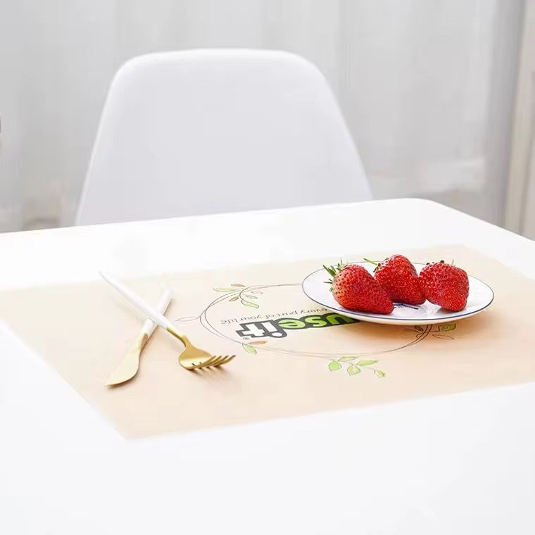 A beige rectangular placemat on a white table, styled with a gold and white fork, a small white plate with three red strawberries, and a white chair in the background.
